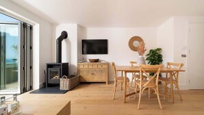 Ein modernes Wohnzimmer mit einem Holzesstisch, Stühlen, einem an der Wand montierten Fernseher, einem Kamin und einem großen Fenster.