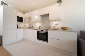 A modern kitchen with white cabinetry, a built-in oven, and a microwave. - Ocean Reach – 2-Bed Sea View Apartment at Tors Park (Lynmouth)