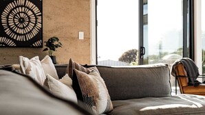 Una sala de estar moderna con un sofá gris, varios cojines, una obra de arte abstracta colgada en la pared y una planta en maceta.