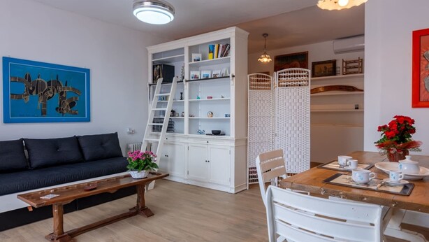 Ein modernes Wohnzimmer mit schwarzem Sofa, Holztisch, weißen Schränken und einem Essbereich mit Holztisch und weißen Stühlen.