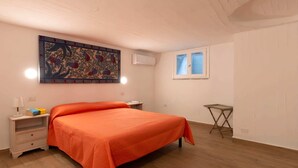 Ein Schlafzimmer mit einem großen Bett, einem Nachttisch, einem kleinen Tisch, einer Wand-Klimaanlage und einem Fenster mit Jalousien.