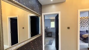 Un pasillo con un espejo grande, un panel decorativo negro y una puerta que da a un dormitorio.
