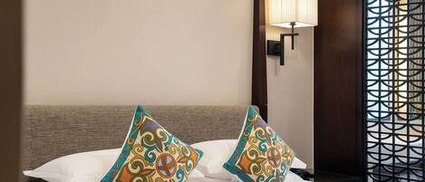 Una camera d'albergo con un letto, due cuscini decorativi, una lampada a parete e un pannello decorato.