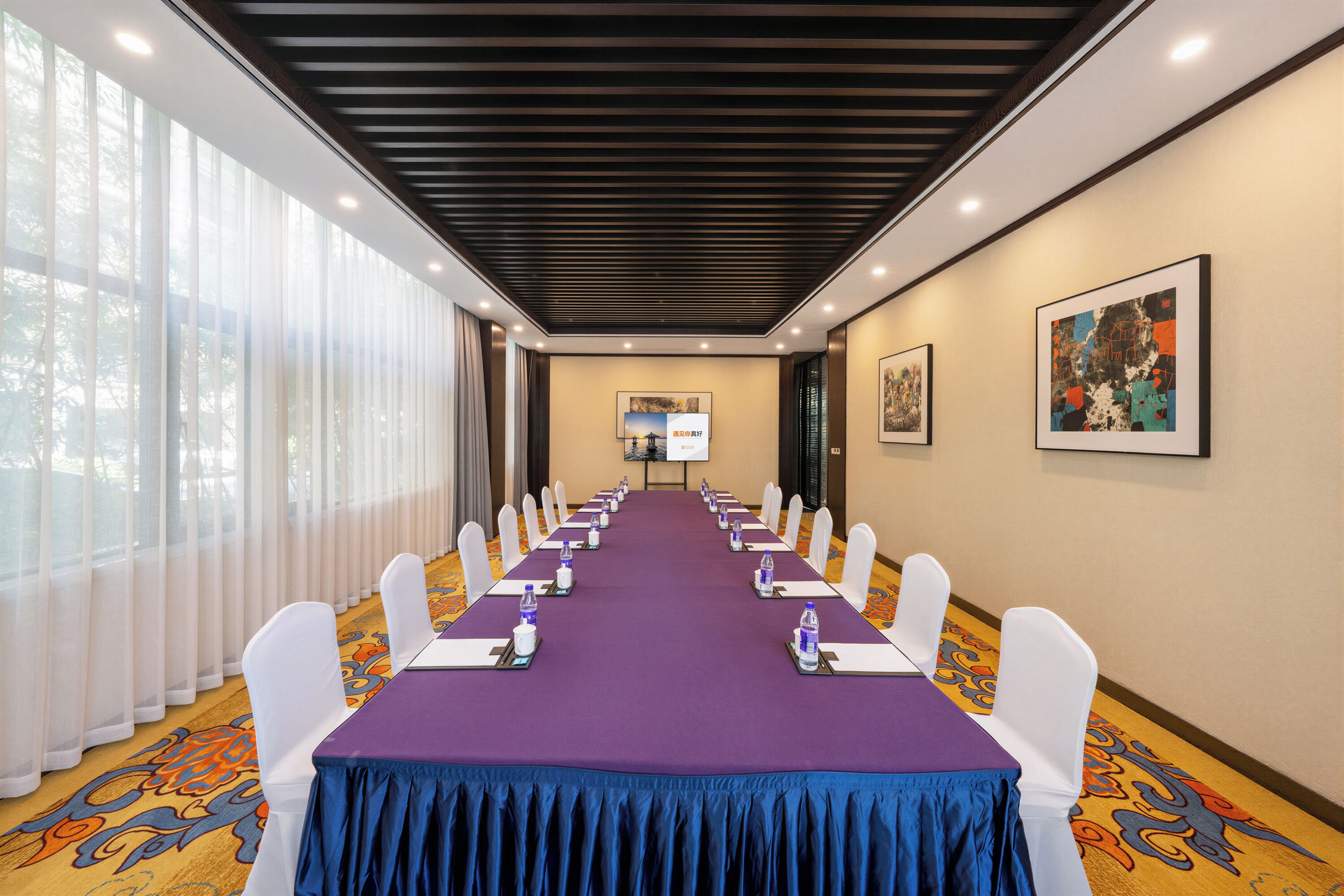 A conference room with a long table, white chairs, and a projector screen at the front.