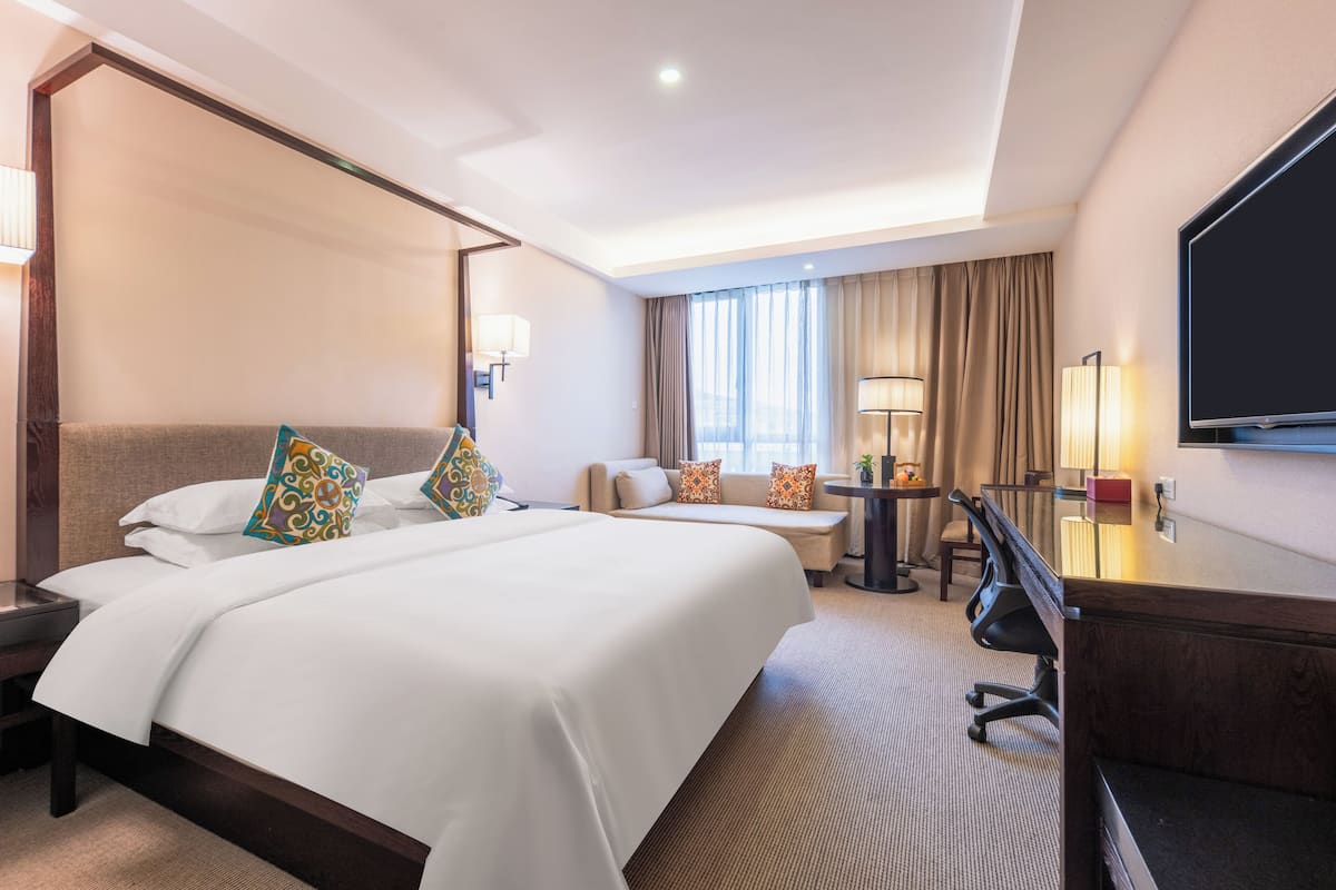 Ein Hotelzimmer mit einem großen Bett, einem Schreibtisch, einem Sessel und einem Fernseher.