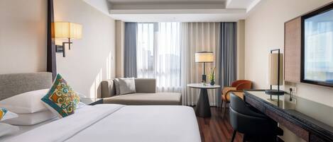 A hotel room with a bed, a desk, a chair, a TV, and a window with curtains.