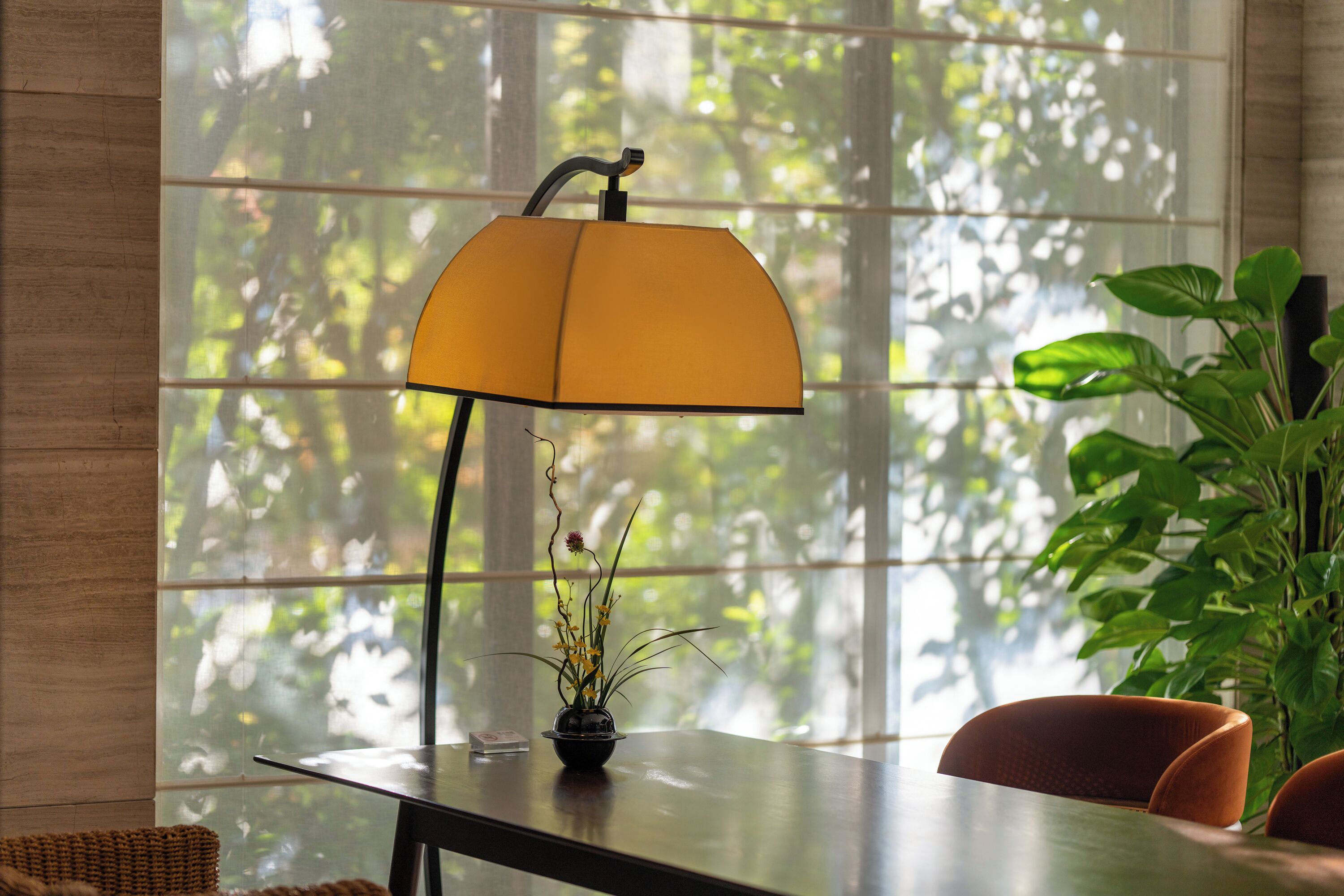 Una mesa con una lámpara, una planta en maceta y una silla en una habitación con un ventanal grande.