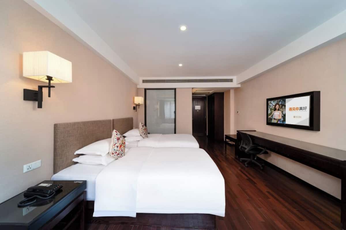 Ein Hotelzimmer mit zwei Betten, einem Schreibtisch mit Telefon, einem Sessel, einer Schreibtischlampe und einem gerahmten Bild an der Wand.
