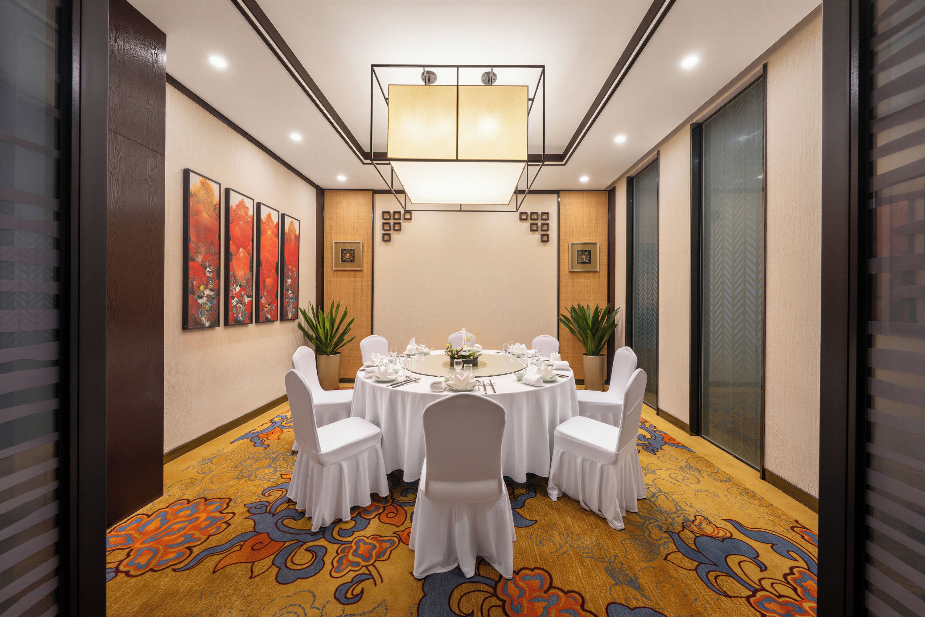 A conference room with a round table set for a meeting, surrounded by chairs, with a patterned carpet and artwork on the walls.