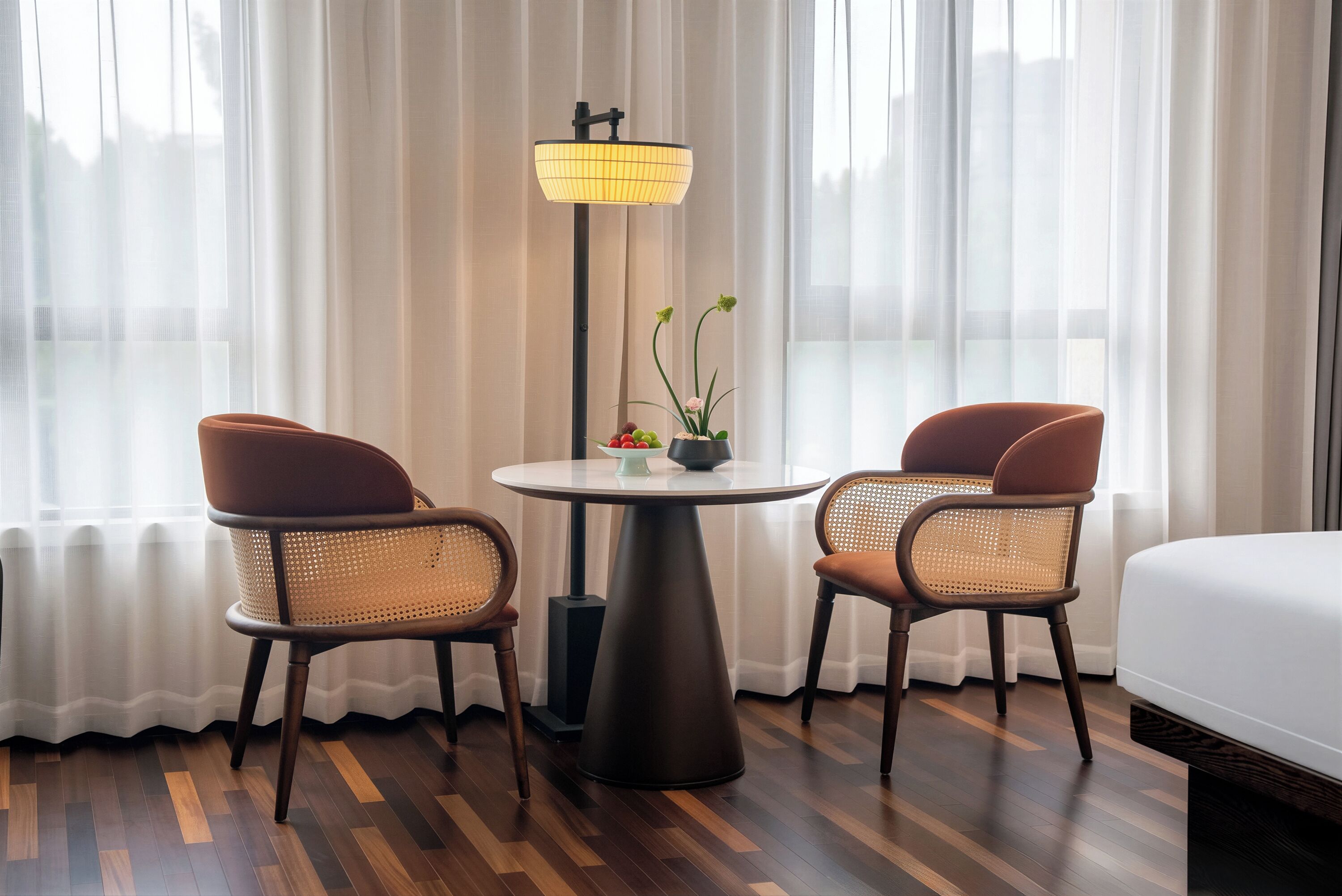 Habitación de hotel con cama, dos sillones, una mesa, una lámpara y una planta en maceta.