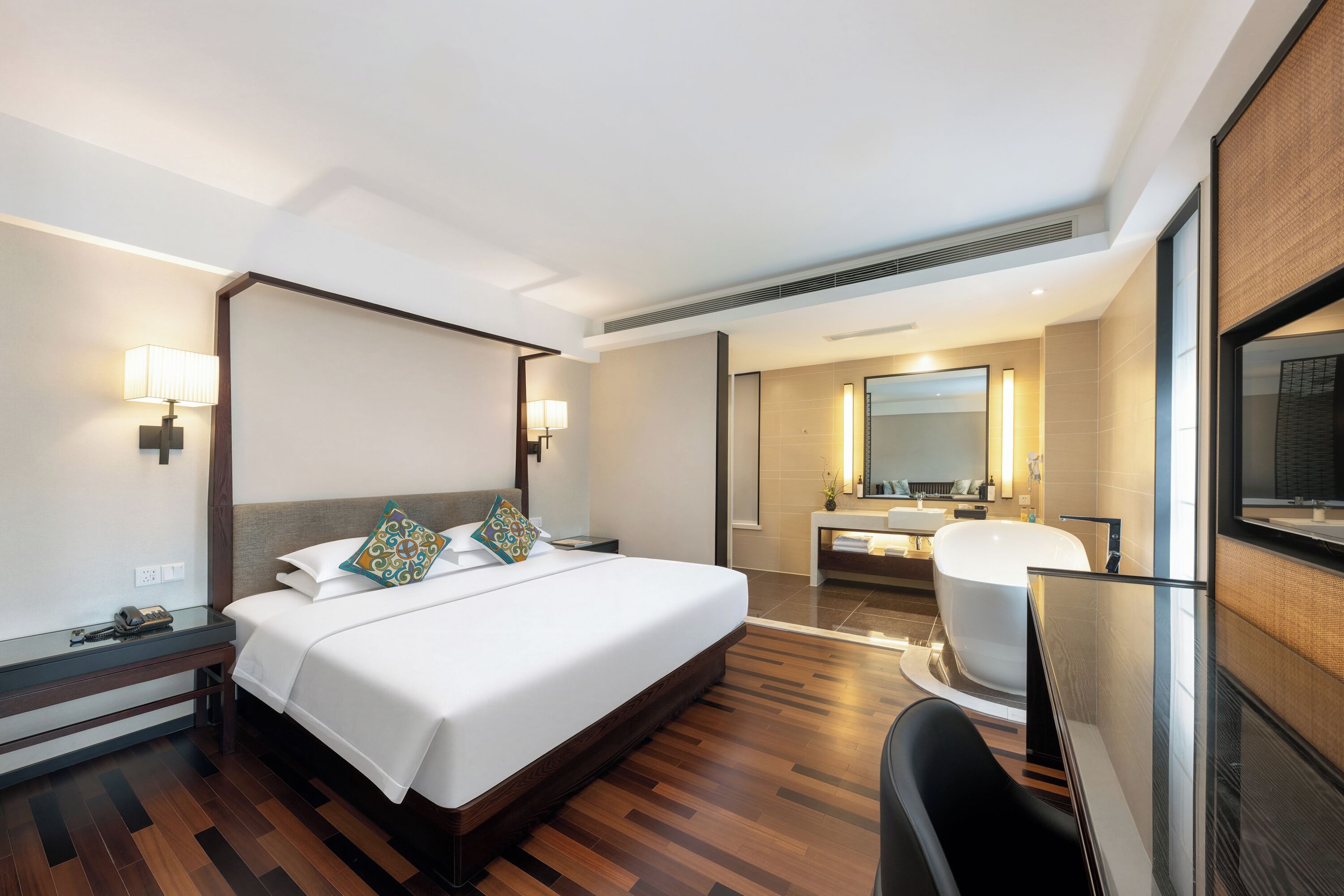 Habitación de hotel con una cama grande, lámparas de noche, un escritorio con teléfono, baño con bañera y un espejo.