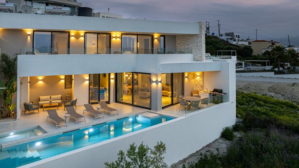Ein modernes, zweistöckiges Haus mit Swimmingpool, Sitzgelegenheit im Freien und Meerblick.