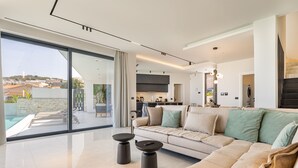 Ein modernes Wohnzimmer mit einem großen Fenster, einem Sofa und einer Küche im Hintergrund.
