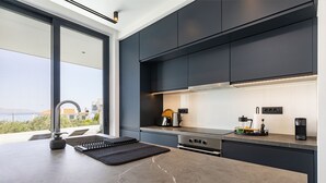 Eine moderne Küche mit dunklen Schränken, einer Edelstahl-Dunstesse und Blick aufs Meer.