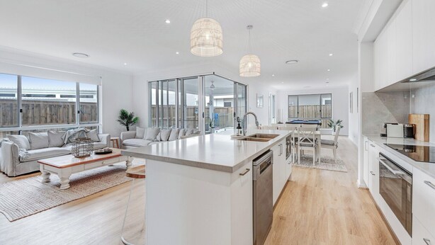 Una cocina moderna con una isla central, armarios blancos y un amplio ventanal con vistas a una terraza de madera.