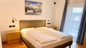 Ein Doppelbett mit Holz-Kopfteil, zwei Nachttische, eine Wandlampe und ein Fenster mit Vorhängen.
