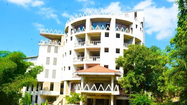 Un edificio de varios pisos con balcones, rodeado de vegetación.