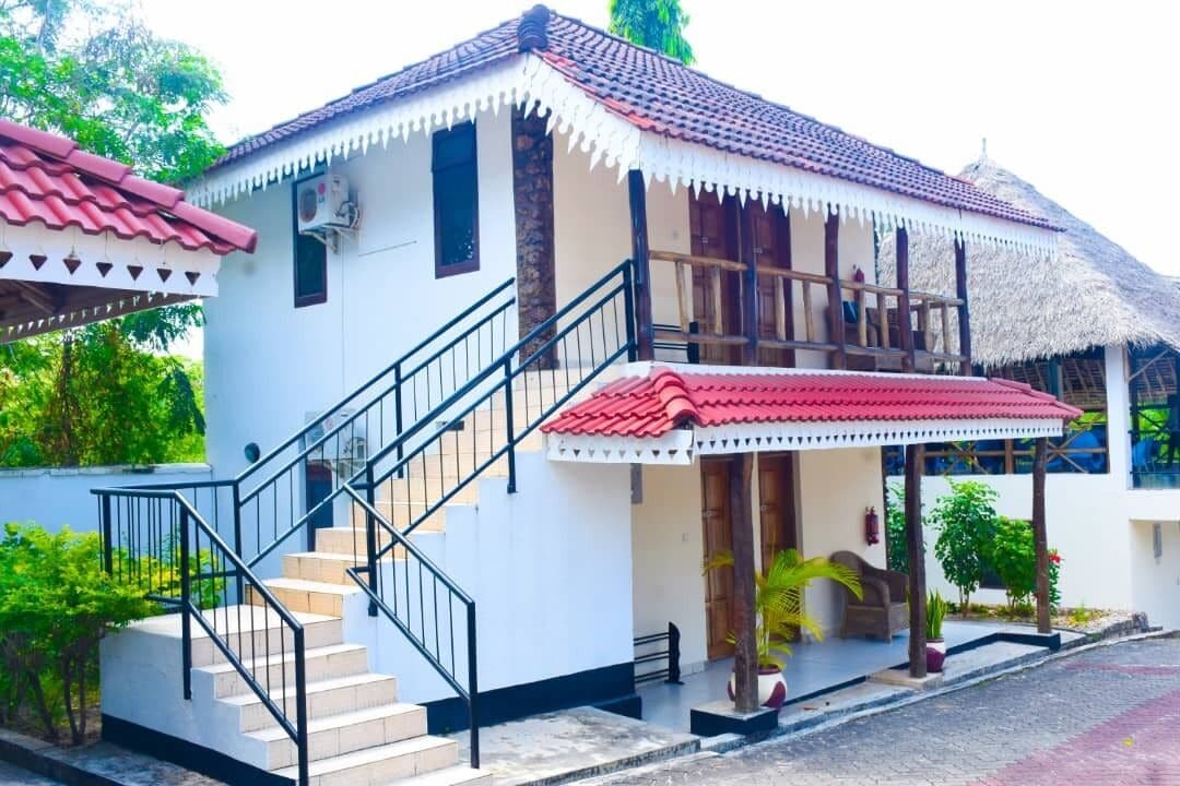 A two-story building with a red-tiled roof, a staircase with black railings, and a covered porch area.