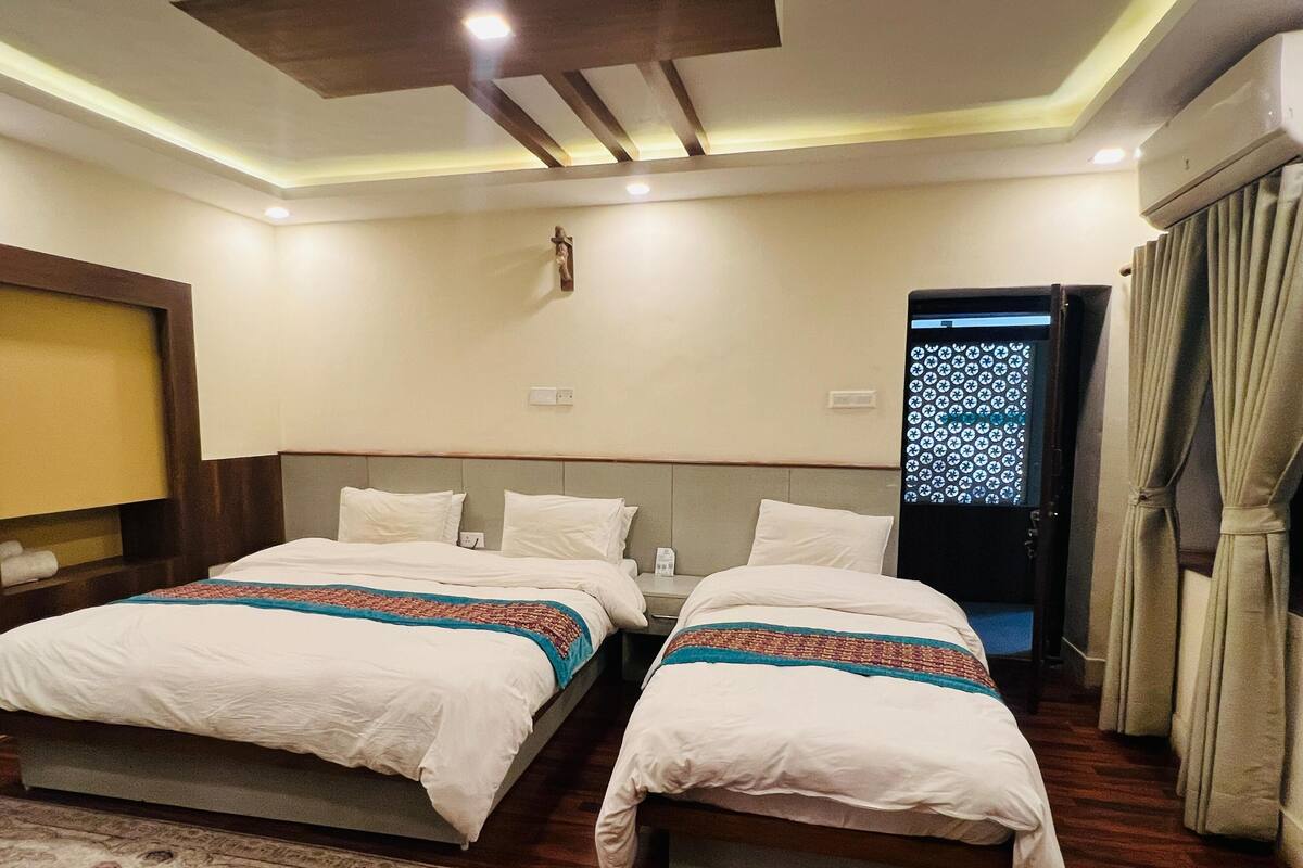 A hotel room with two beds, a wooden floor, a patterned rug, a wall-mounted air conditioner, and a door with a patterned glass panel.