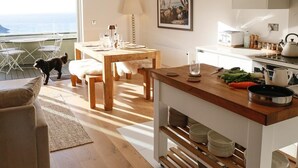A modern kitchen with wooden countertops, a dining area with a table and chairs, and a view of the ocean. - Oceanfront Apartment w/Balcony & Sauna, Pet-Friendly (Lynmouth)