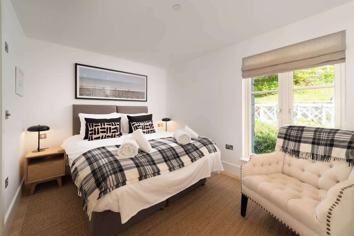 Ein Schlafzimmer mit Bett, Nachttisch, Sessel, Fenster mit Aussicht und einem Bild an der Wand.