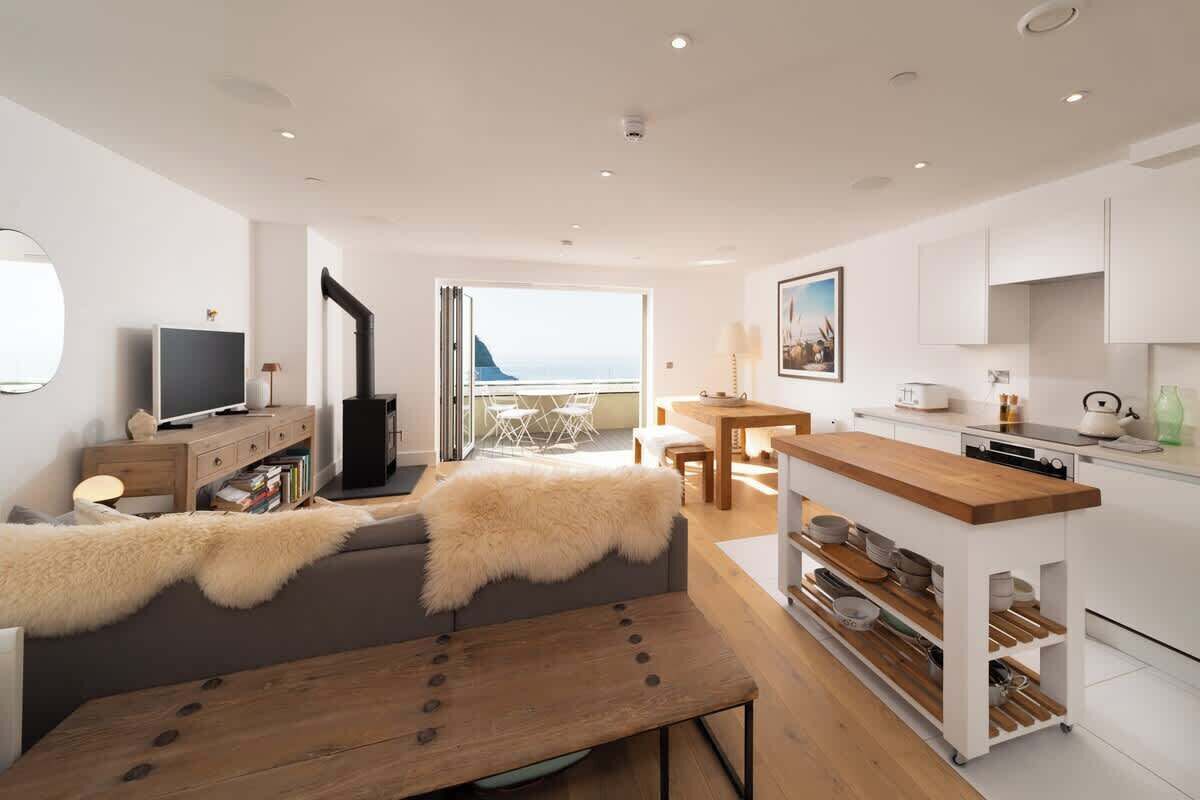 A modern living room with a sofa, a wooden table, and a kitchen area with a wooden countertop and cabinets.
