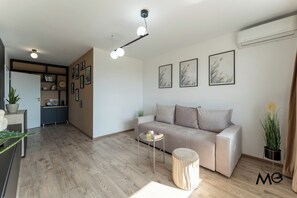 A modern living room with a sofa, a coffee table, and a round ottoman. There are framed pictures on the wall, a ceiling light fixture, and a plant on the floor. - MoHost Noblesse - Urban Style & Comfort (Brașov)