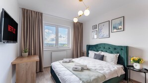 Ein modernes Hotelzimmer mit einem großen Bett, einem Fernseher, der 'NETFLIX' zeigt, einem Fenster mit Blick und einem Nachttisch mit einer Pflanze.