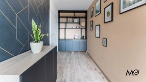 Ein Flur mit dunkler Wand, einer Topfpflanze, einem blauen Schrank und einem Regal mit Büchern und einer Uhr.