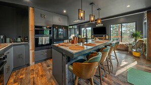 A modern kitchen with a central island, wooden chairs, and hanging pendant lights. - The Sky Loft Boutique (Bailey)