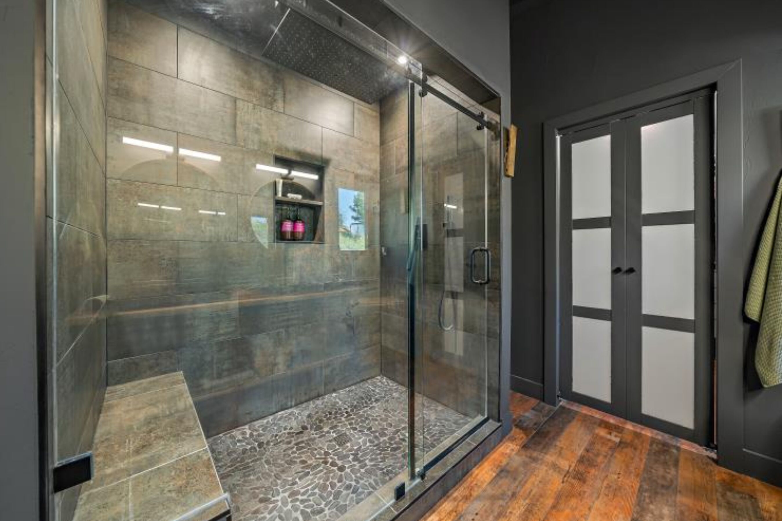 A modern shower area with glass doors, a stone wall, and a wooden floor.