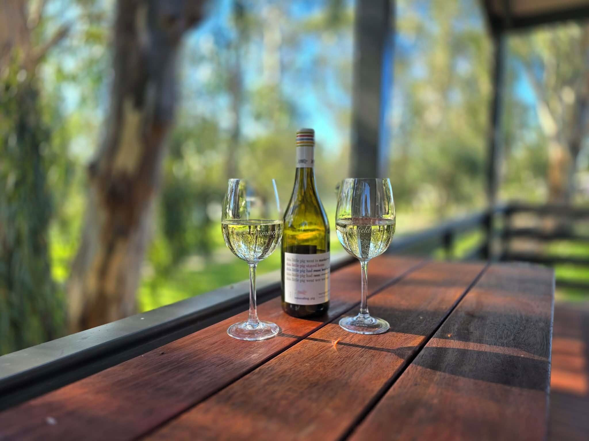 A wooden table with a bottle of white wine and two glasses on it.