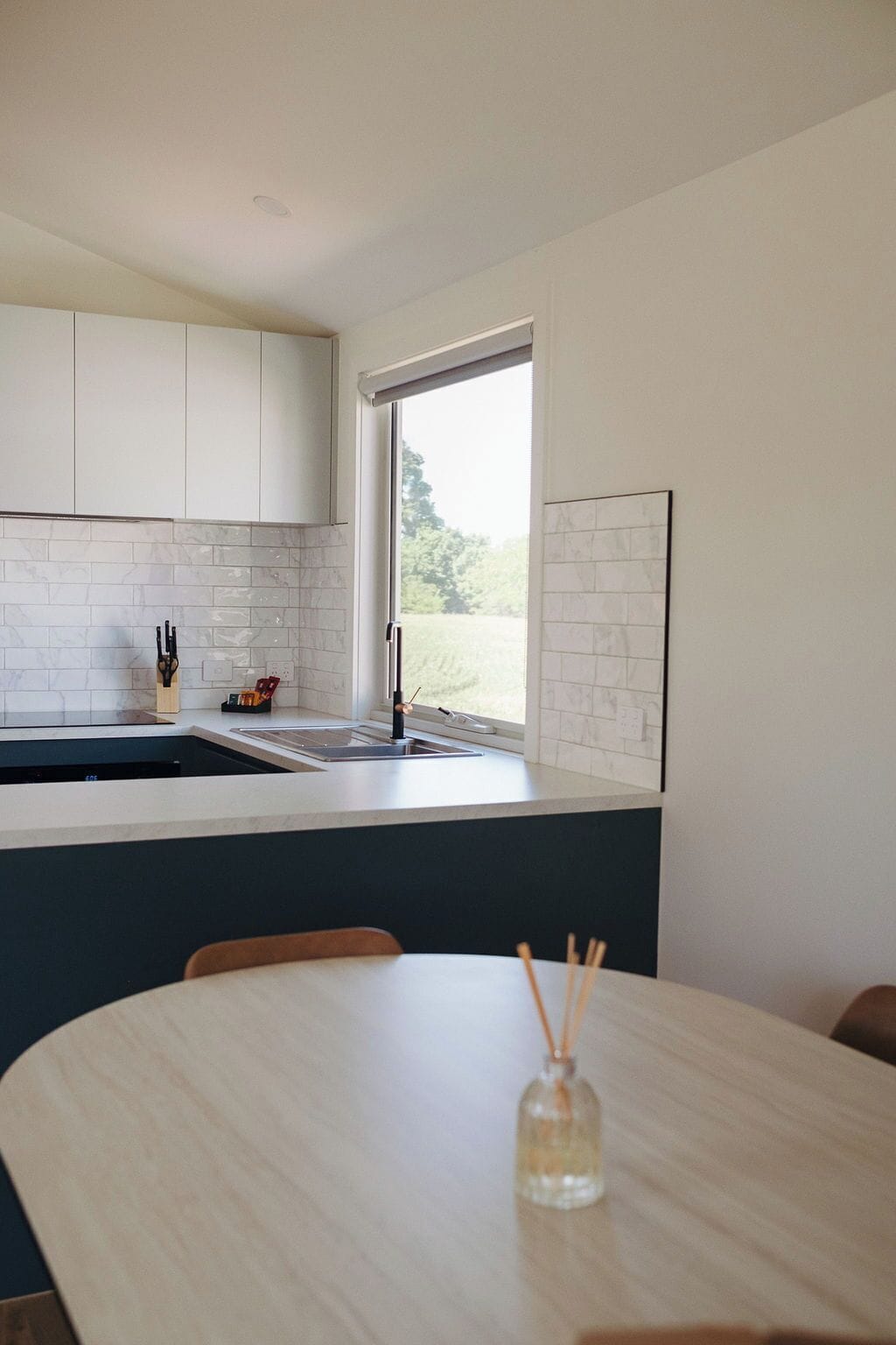 A modern kitchen with white cabinets, a large window, and a dining area with a table and chairs.