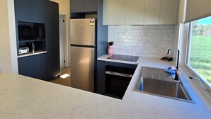 A modern kitchen with a built-in microwave, a stainless steel refrigerator, a dishwasher, and a sink with a window above it. - Bridgewater Caravan Park (Bridgewater on Loddon)