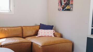 A living room with a brown leather sofa, a small table with a glass vase, and a colorful abstract painting on the wall.
