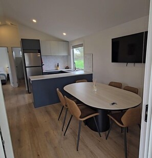 A modern kitchen with a central island, a dining area with a round table and chairs, and a flat-screen TV mounted on the wall. - Bridgewater Caravan Park (Bridgewater on Loddon)