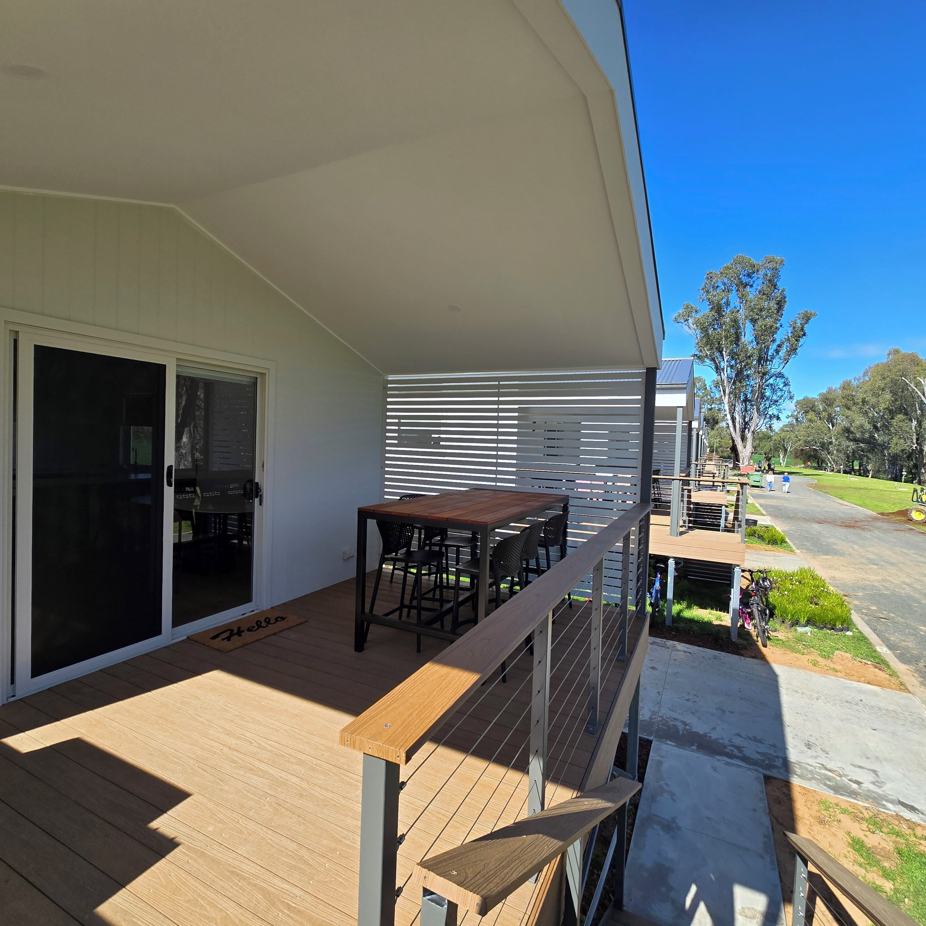 A covered outdoor area with a wooden deck, a table with chairs, and a sliding glass door leading to an interior space.