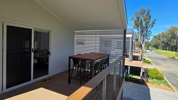 A covered outdoor area with a wooden deck, a table with chairs, and a sliding glass door leading to an interior space.