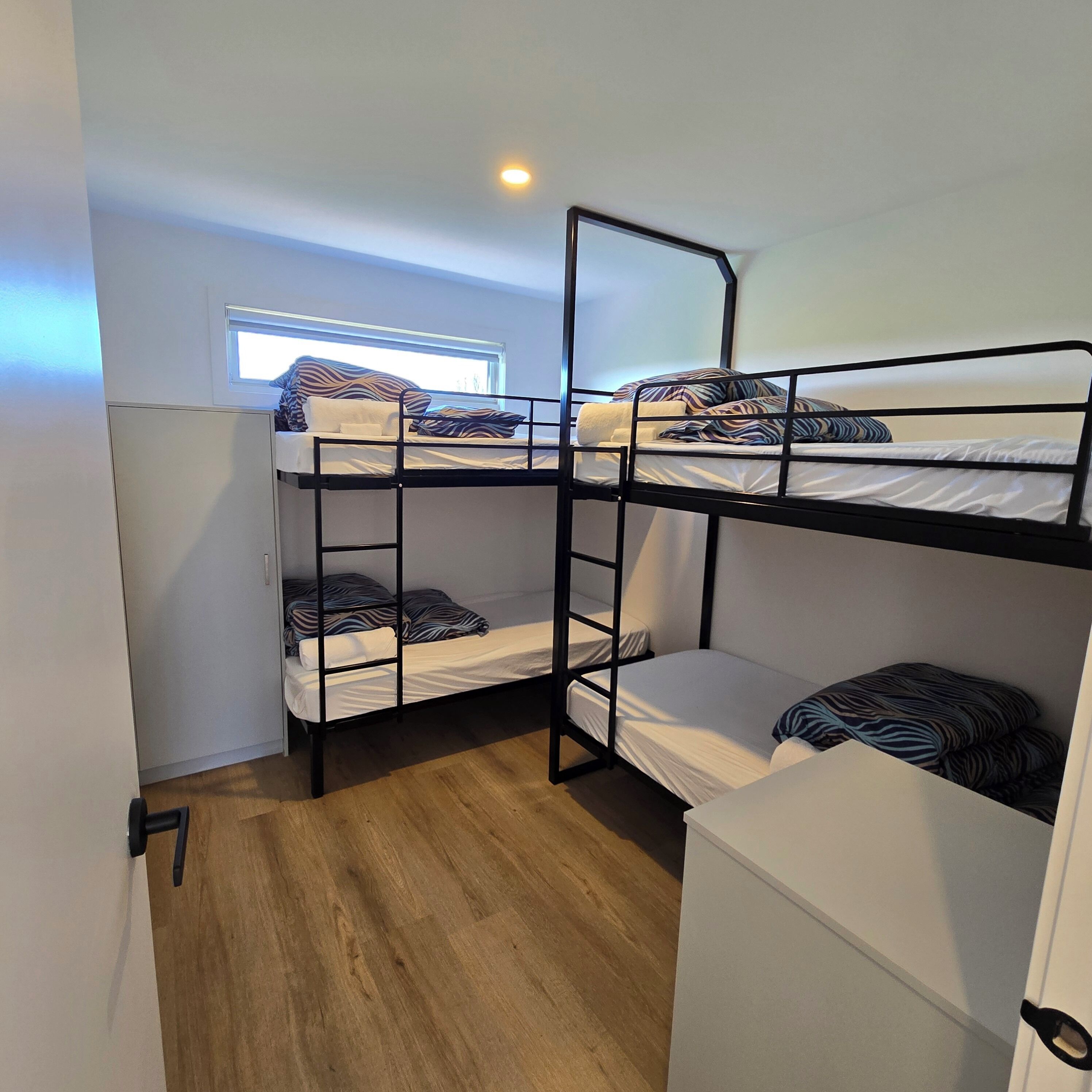Habitación con literas, ventana, suelo de madera y una puerta.