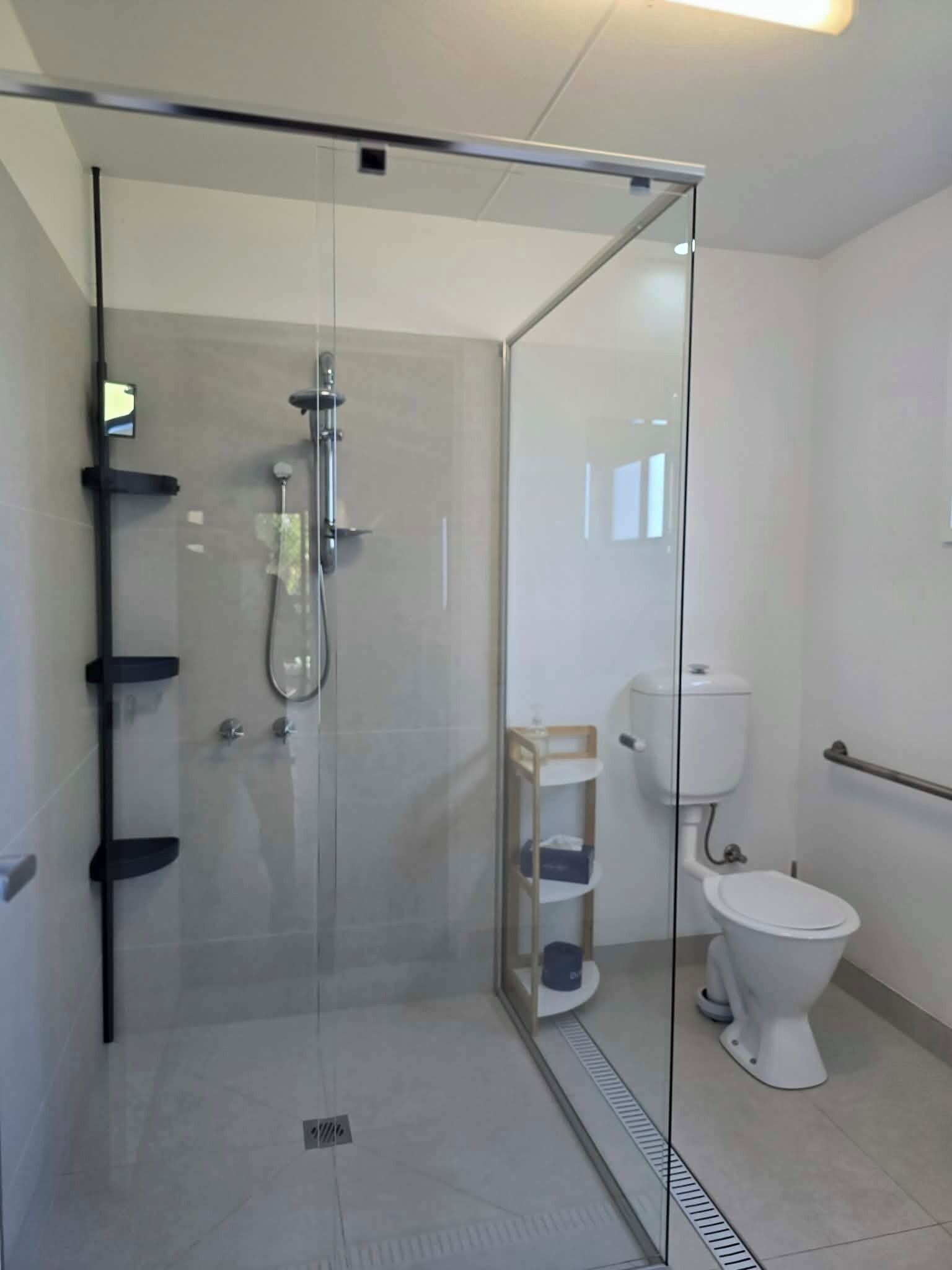 Une salle de bain moderne avec une douche à parois de verre, des toilettes et une petite étagère.