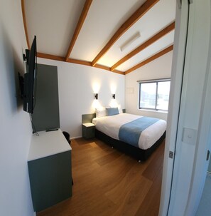 A bedroom with a bed, bedside lamps, a TV mounted on the wall, and a window. - Bridgewater Caravan Park (Bridgewater on Loddon)