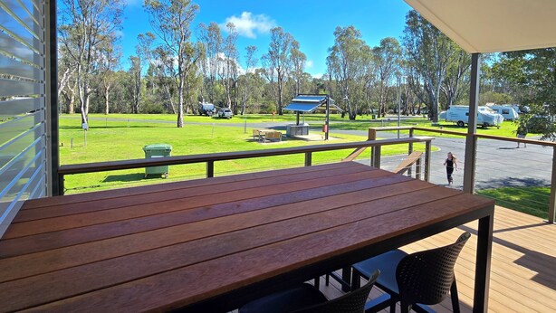A wooden deck with a table and chairs, overlooking a park with picnic tables and RVs. - Bridgewater Caravan Park (Bridgewater on Loddon)