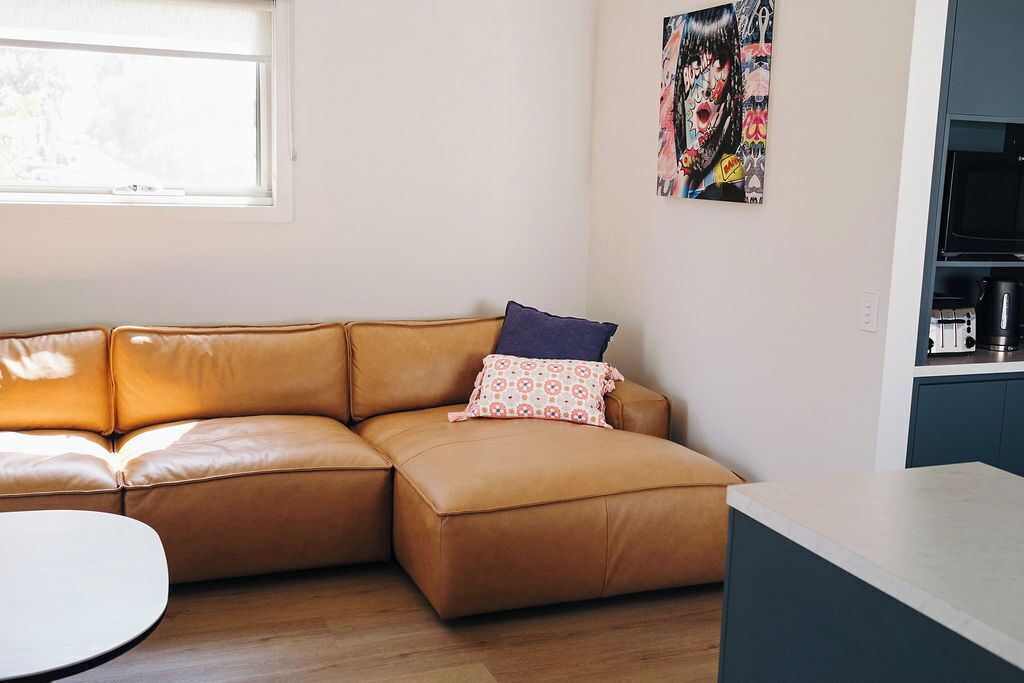 Una sala de estar moderna con un sofá de cuero marrón, una mesita redonda y una zona de cocina con un microondas.