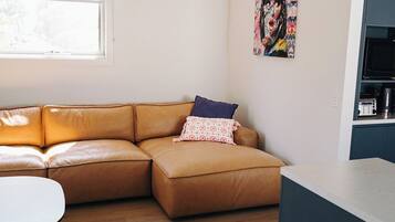 Una sala de estar moderna con un sofá de cuero marrón, una mesita redonda y una zona de cocina con un microondas.