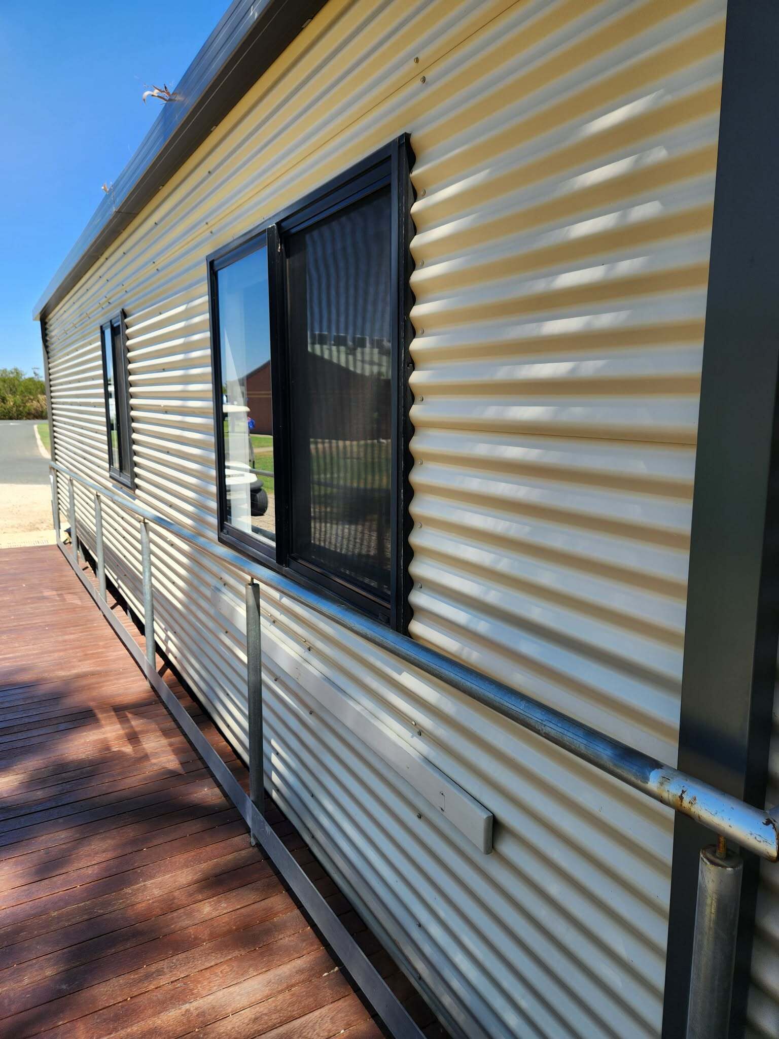 Une maison mobile avec une façade en métal, une terrasse en bois et une fenêtre dotée d’un cadre noir.