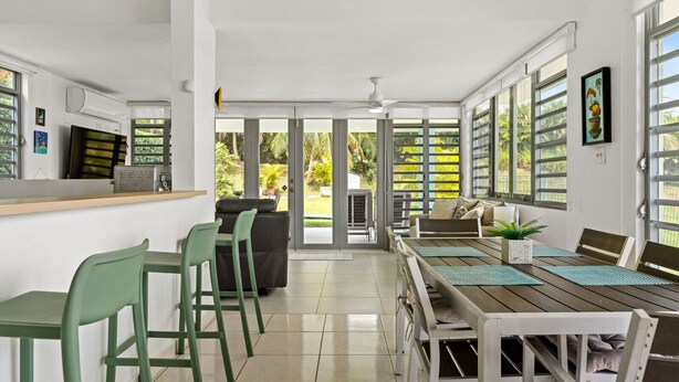 Una cocina moderna con estufa integrada, un comedor con mesa y sillas de madera, y grandes ventanales con vistas al exterior.