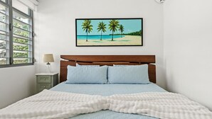 Un dormitorio con una cama, una mesita de noche, una lámpara y un cuadro de una playa.