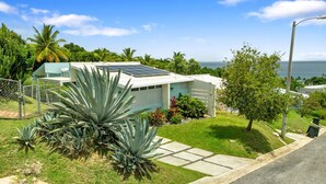 Una casa con paneles solares, un césped cuidado y vista al océano.