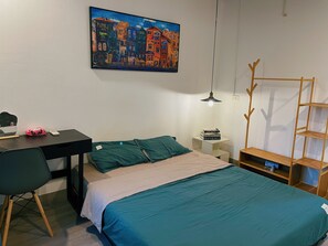 A bedroom with a bed, a desk, a chair, a bookshelf, and a painting on the wall.