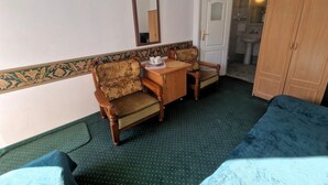 Een kamer met een bed, twee stoelen, een klein tafeltje met kop en schotel, een spiegel en een kledingkast.